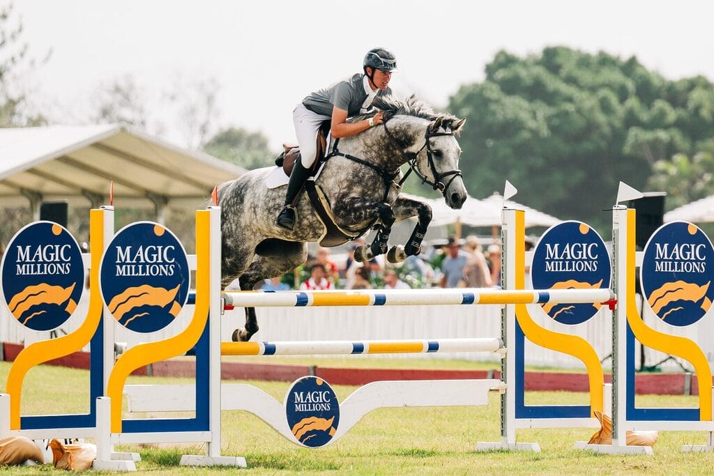A rider and grey horse clearing a Magic Millions showjumping fence